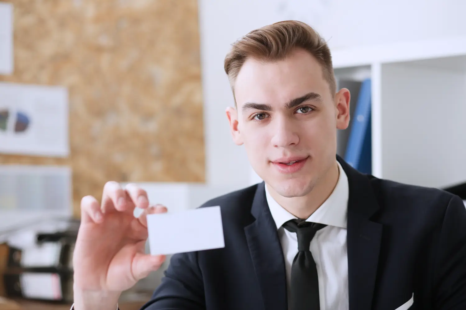 Lächelnder Geschäftsmann im Anzug hält eine leere Visitenkarte in der Hand, Nahaufnahme.